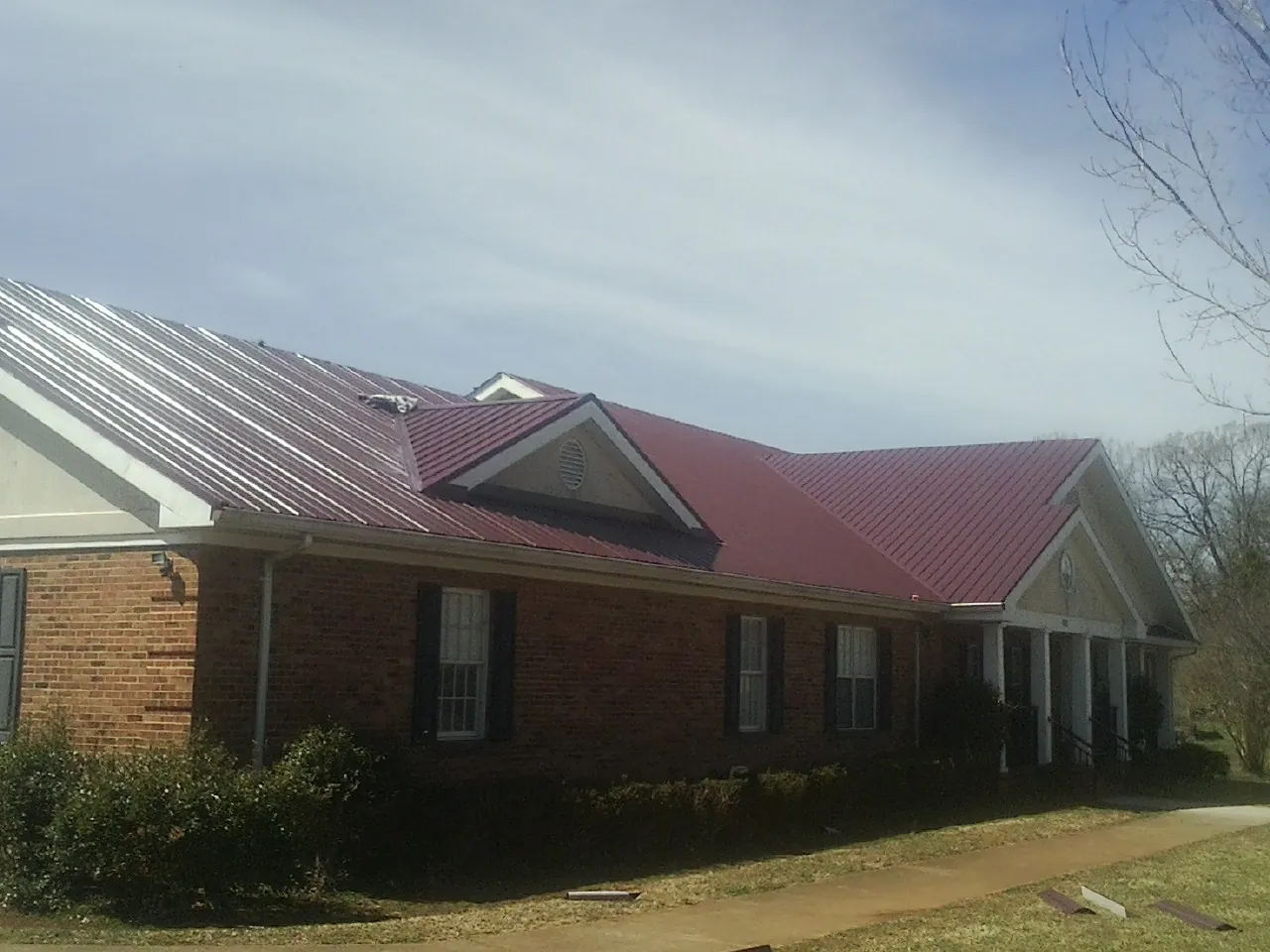 Red metal roof with gabled entries on a long brick building, from a Hail Damage Roof Repair job in Towson