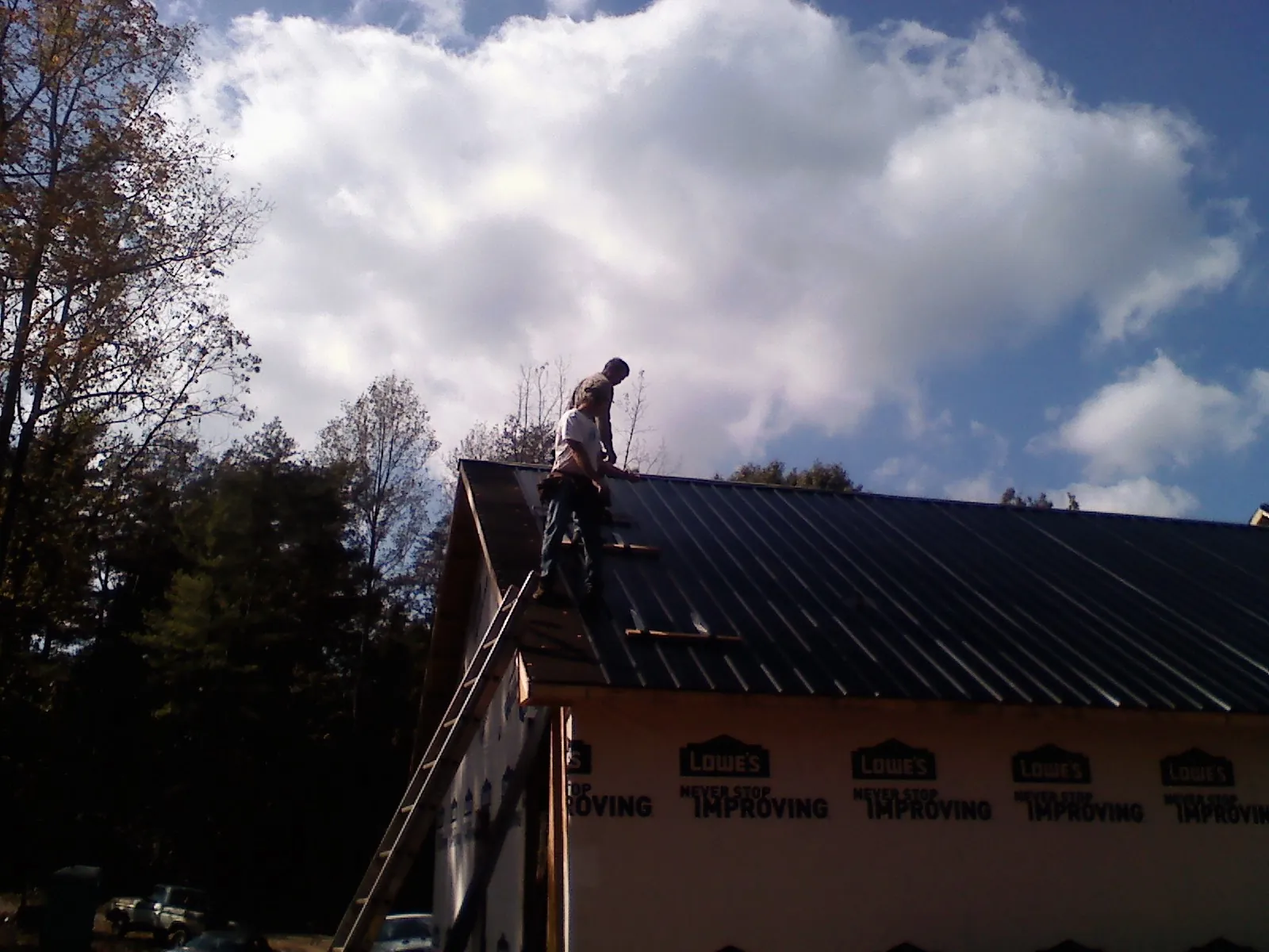 Roofer fastening dark metal panels high against a cloudy sky, from a Roof Inspection job in Towson